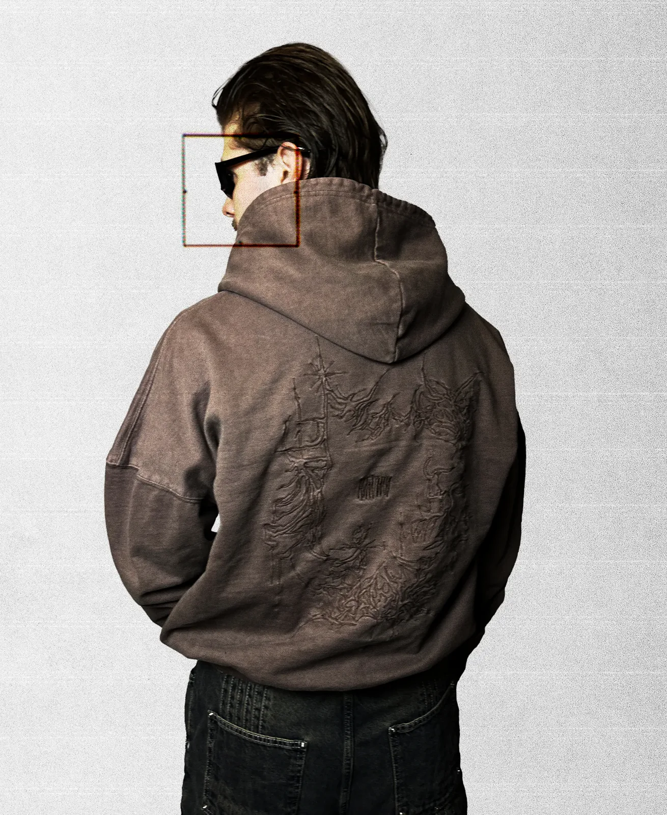Model seen from behind in a washed mocha zip hoodie with large tonal embroidery across the back