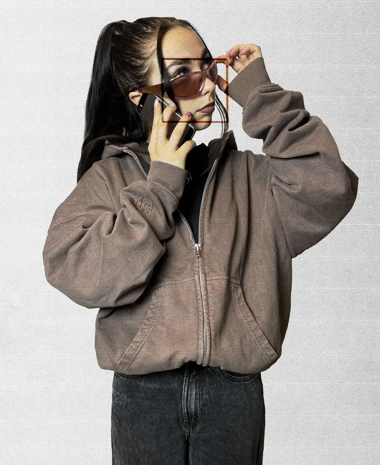 Model in a washed mocha zip hoodie, phone to one ear, adjusting a pair of pink sunglasses